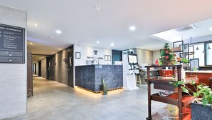 Zona de recepción de hotel con mostrador de mármol, un escritorio de recepción, un árbol de Navidad y un directorio en la pared.