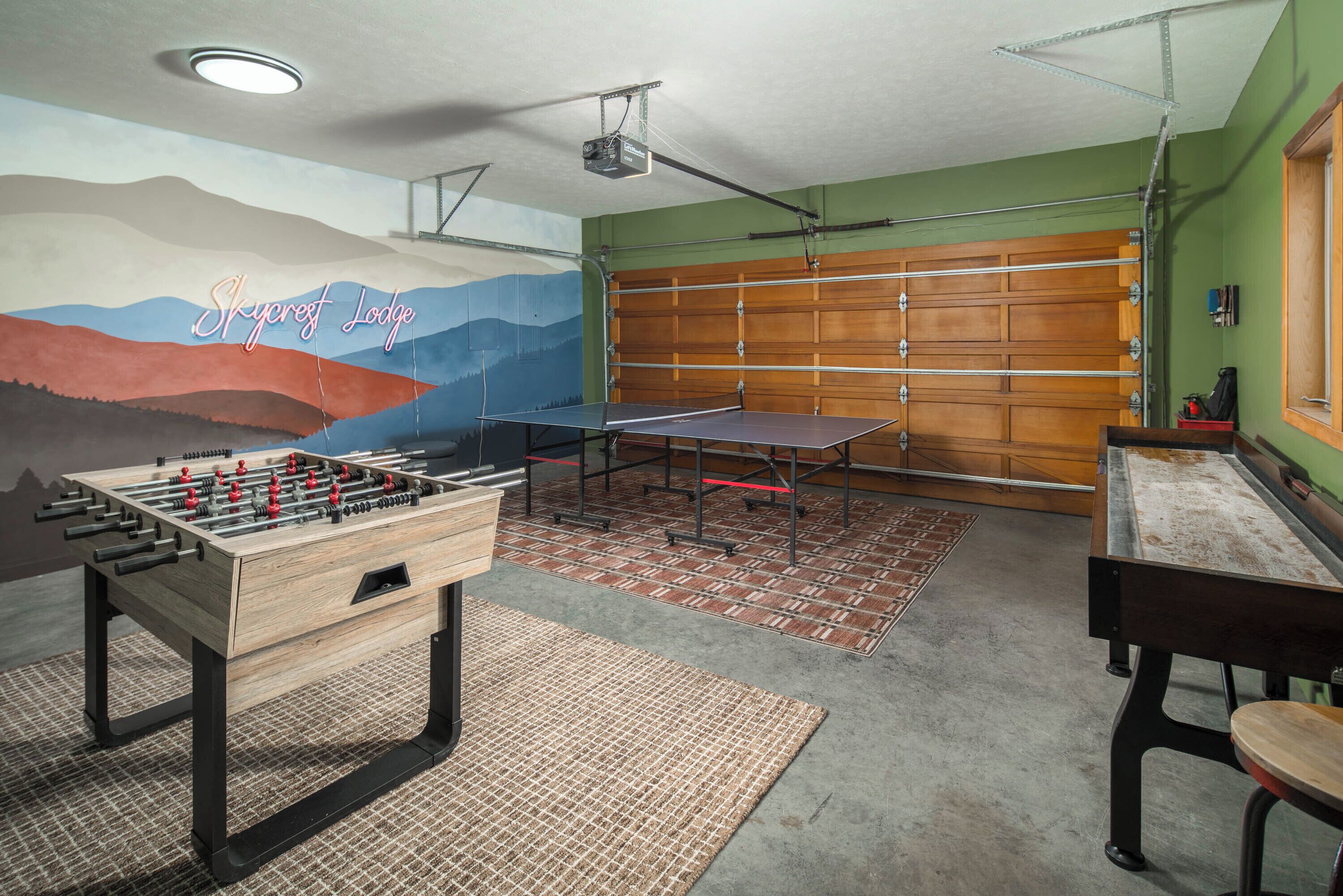 Una habitación con mesa de fútbol de mesa, mesa de ping pong y un mural de montañas.