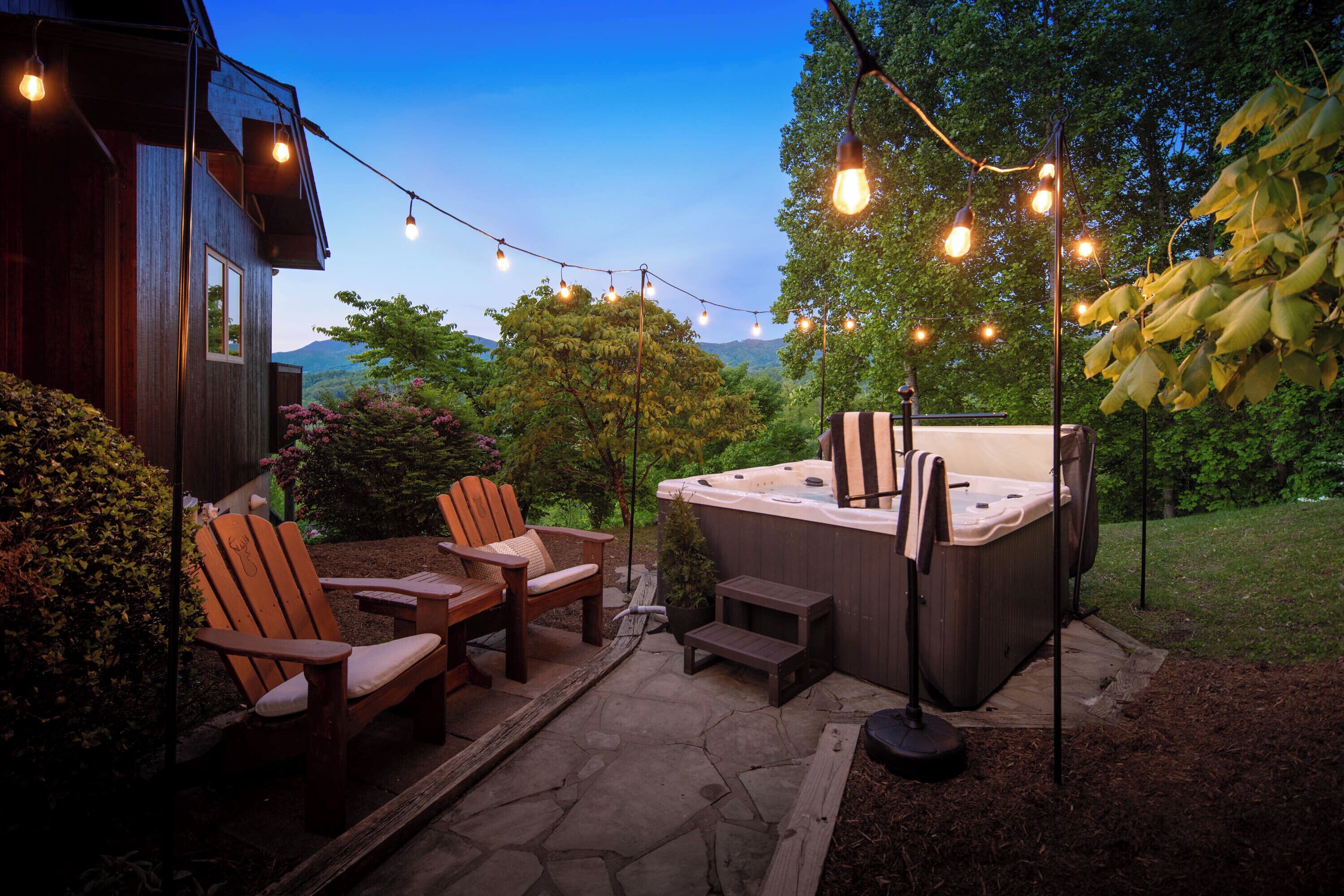 Une terrasse extérieure avec des chaises en bois, un jacuzzi et des guirlandes lumineuses.