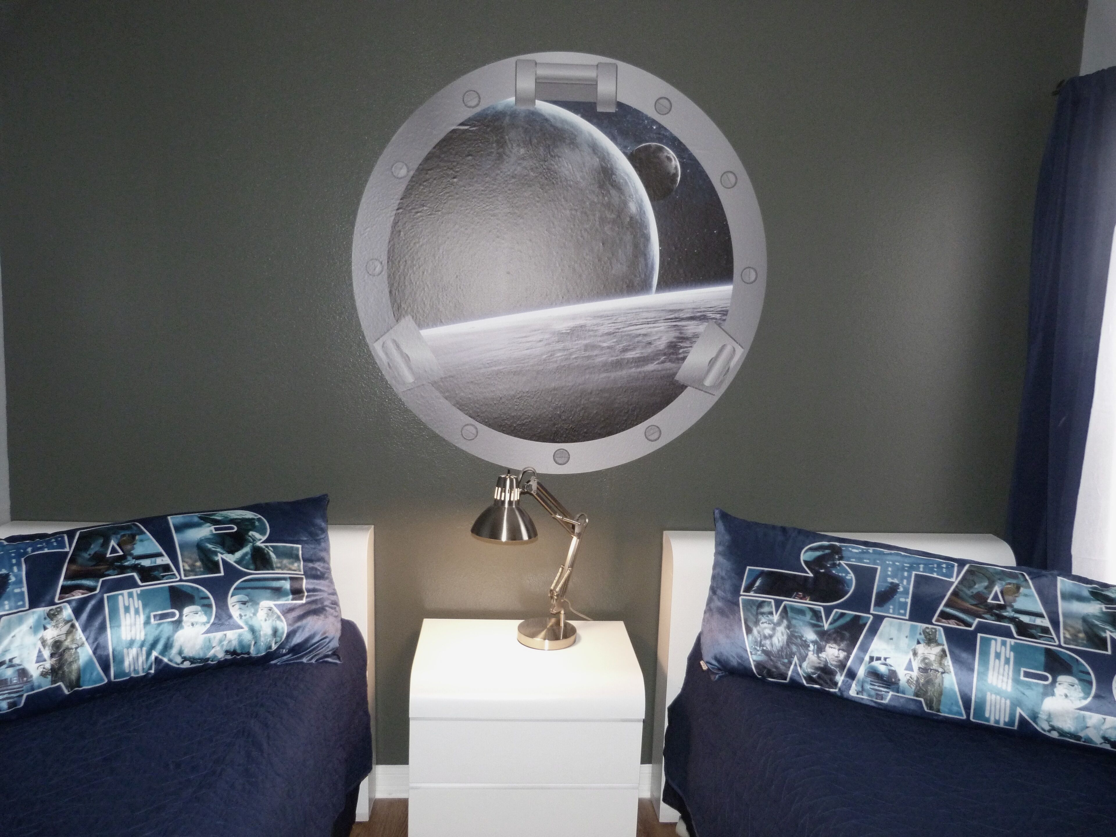 Een slaapkamer met twee bedden, elk voorzien van een Star Wars-thema kussen, een nachtkastje en een spiegel aan de muur met een ruimte-thema ontwerp.