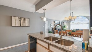 Eine moderne Küche mit Granit-Arbeitsplatten, Spüle aus Edelstahl und einem Essbereich mit Holzkohle und einer Pendelleuchte.