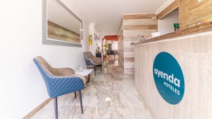 Et receptionområde med et blåt skilt for Ayenda Hotels, en disk med et spejl og siddepladser med en blå stol og et lille bord.