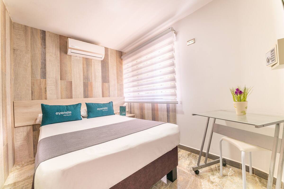 A hotel room with a bed, a desk, and a window with blinds.