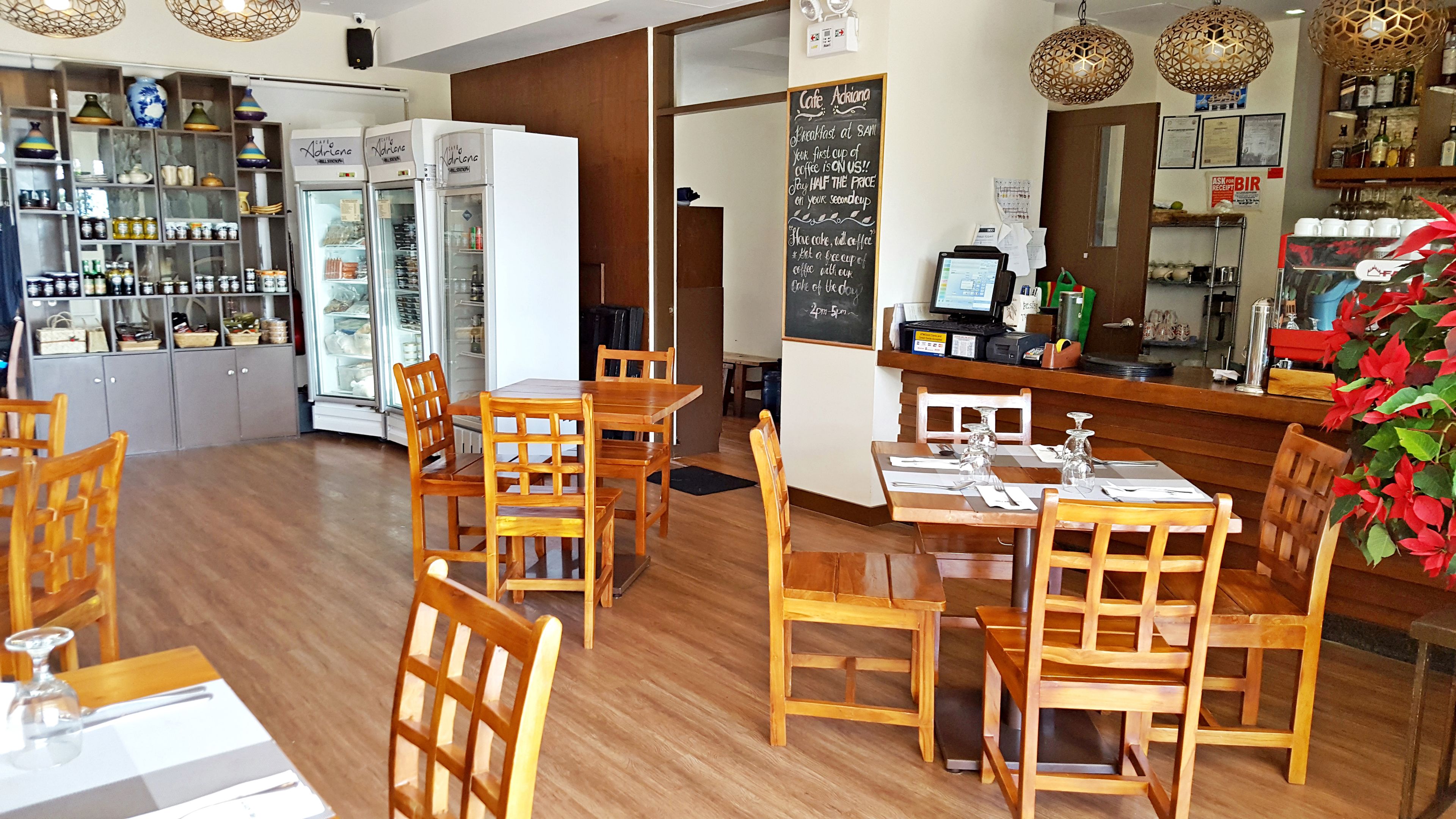 Una cafetería con mobiliario de madera, un menú en una pizarra y un refrigerador lleno de bebidas.
