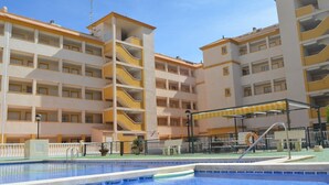 Un hotel de varios pisos con piscina, balcones y una zona cubierta con asientos.