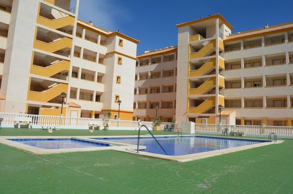A multi-story hotel with balconies, a pool area, and a green lawn.