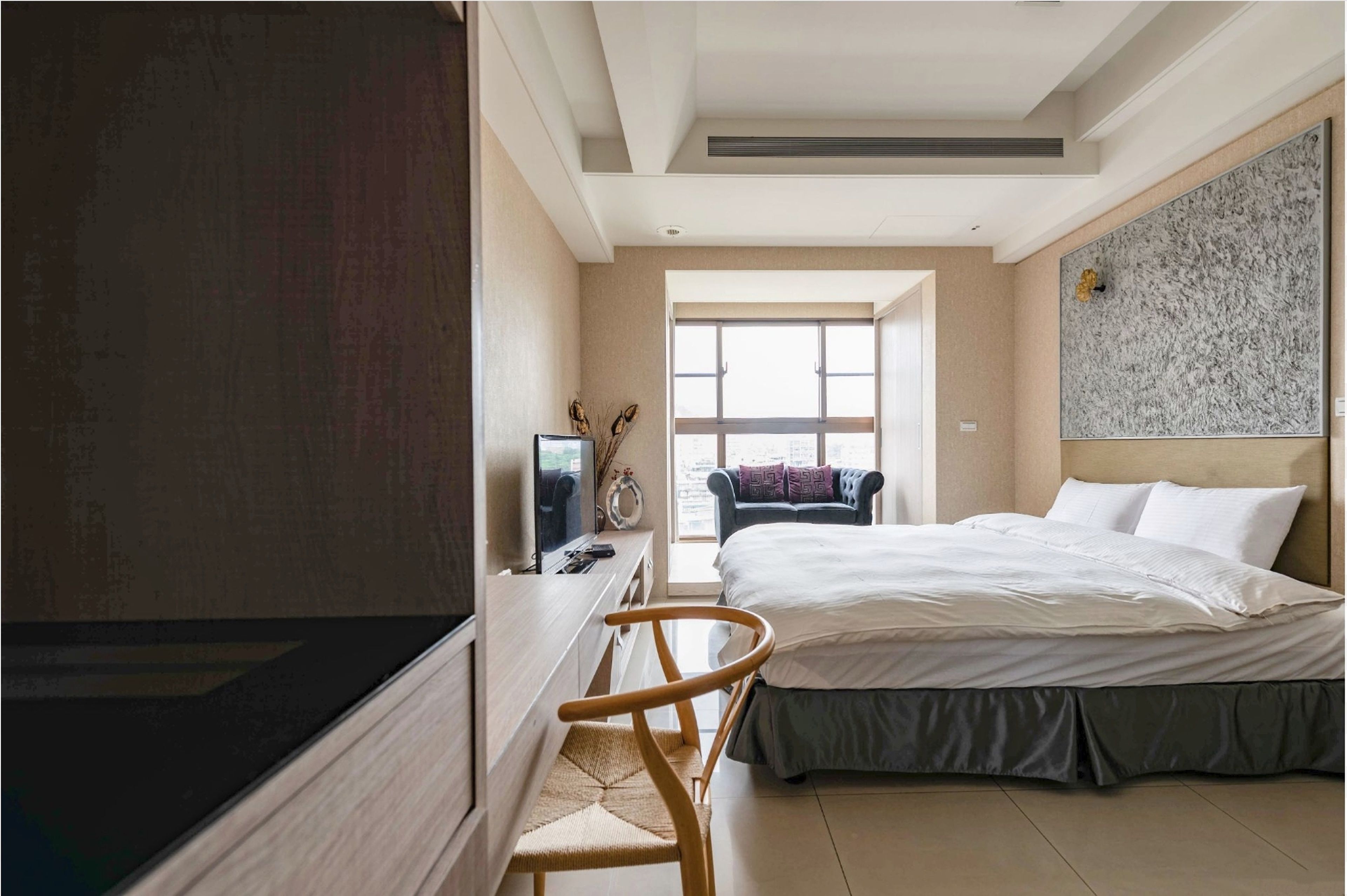 A hotel room with a bed, a desk with a computer, a chair, a TV, and a large window.
