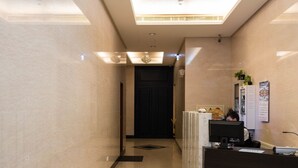 Uma área de recepção de hotel com balcão, um banco e um lustre.
