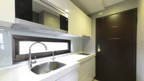 Cozinha moderna com armários brancos, pias de aço inoxidável e porta escura.