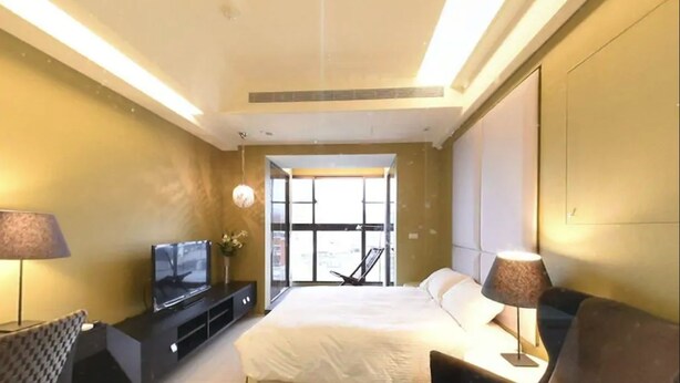 Quarto de hotel moderno com uma cama grande, televisão de tela plana, escrivaninha com luminária e vista através de uma janela ampla.