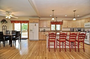 A spacious kitchen with wooden cabinets, a central island with bar stools, a refrigerator, and a dining area with a table and chairs.