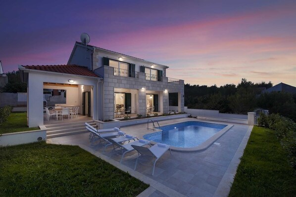 Uma casa moderna de dois andares com piscina, área de estar ao ar livre e um jardim bem cuidado.