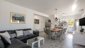 Ein modernes Wohnzimmer mit einer schwarzen Ledersofa, einem Esstisch mit Stühlen und einer Küchenzeile mit weißen Schränken und einem großen Fenster.