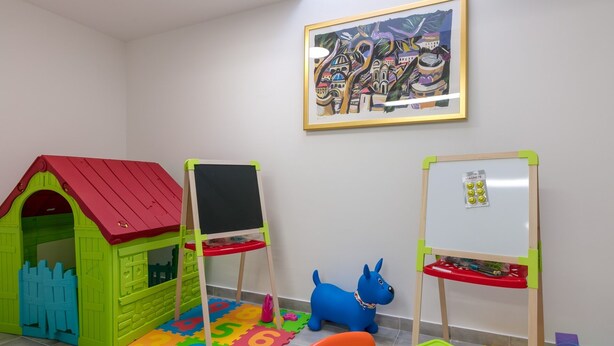 Ein Spielzimmer mit einem grünen Spielhäuschen, zwei Whiteboards, einem blauen Spielzeughund und einer bunten Krabbeldecke.