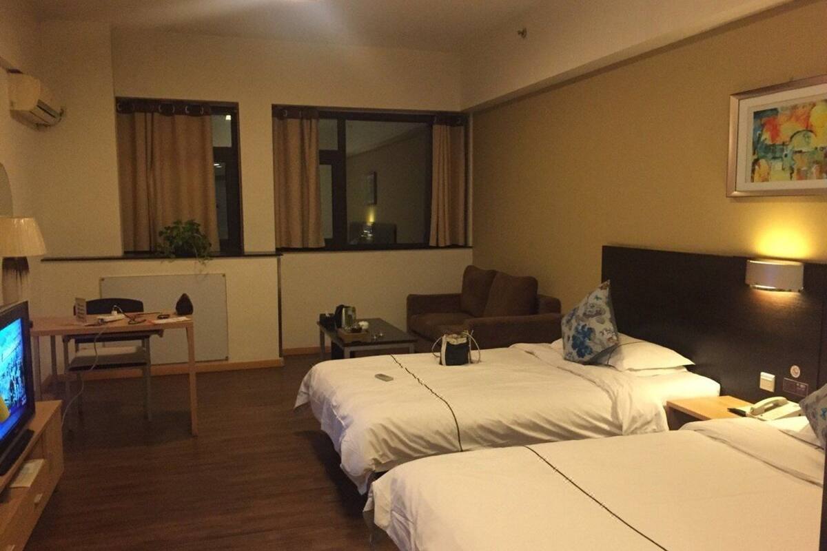 Habitación de hotel con dos camas, un escritorio, una silla, un televisor y una ventana con cortinas.