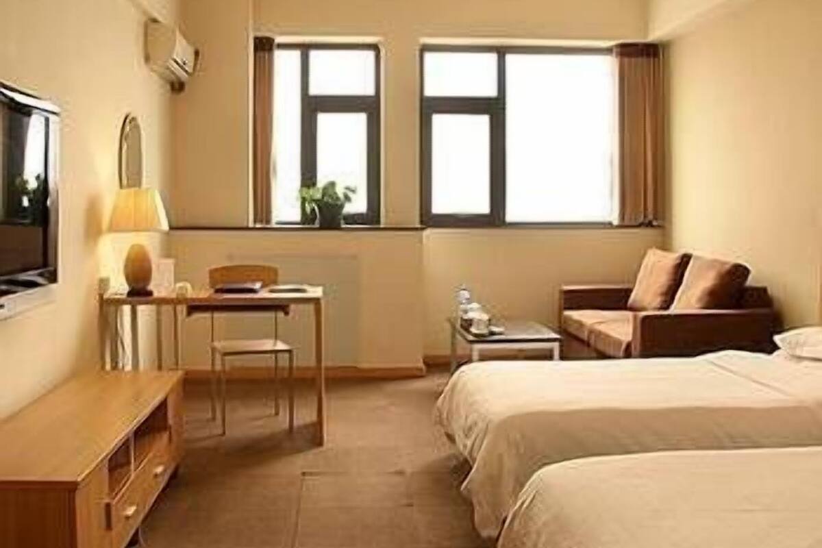 Habitación de hotel con dos camas, un escritorio, una silla, un televisor y dos ventanas.