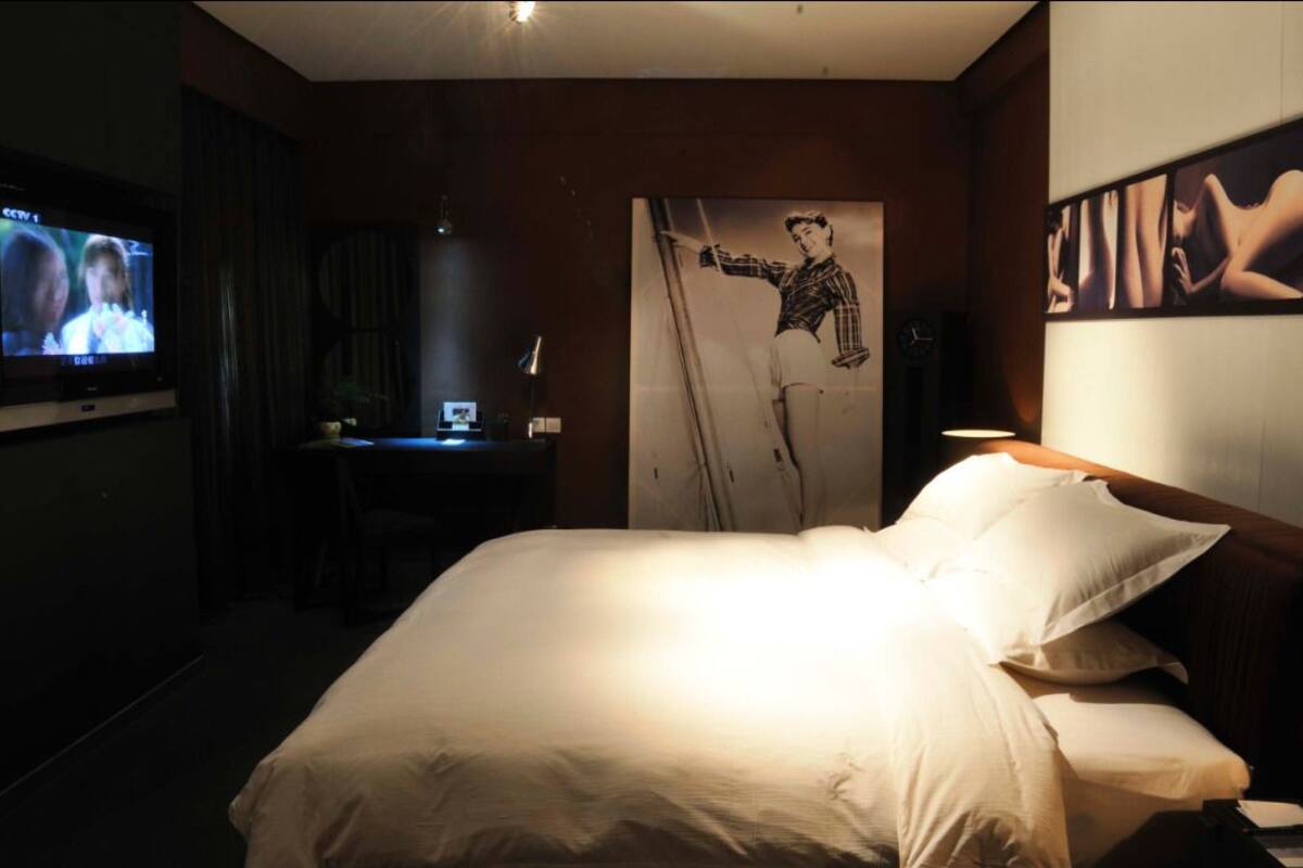 Habitación de hotel con cama, escritorio con computadora, televisión y obras de arte en las paredes.