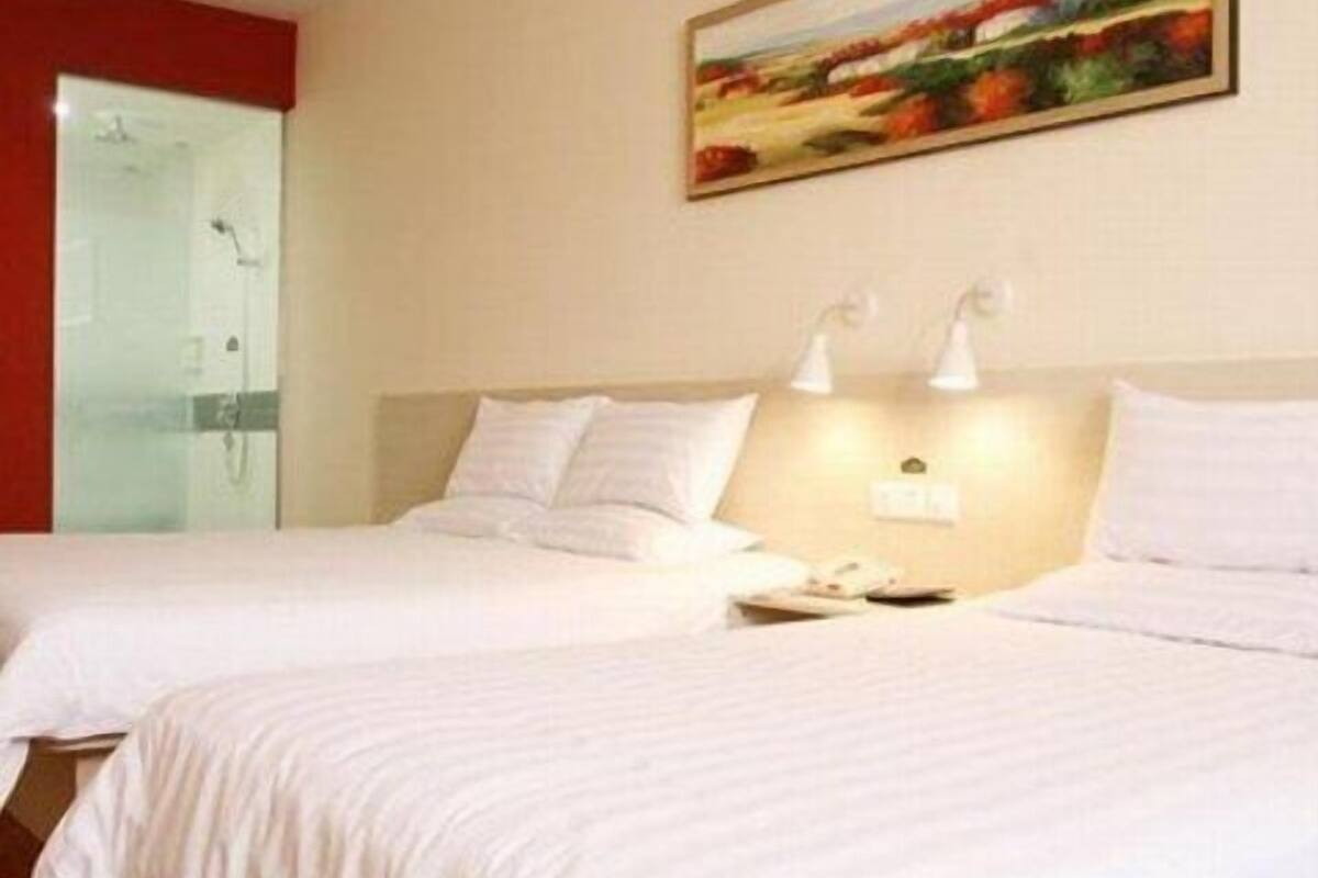 Habitación de hotel con dos camas, un cuadro en la pared y un baño con cabina de ducha de vidrio.