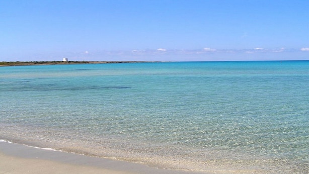 A beach with clear turquoise water and a sandy shore.