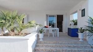 A white exterior with a stone staircase leading to a door, white outdoor furniture, and potted plants.