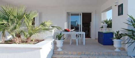 A white exterior with a stone staircase leading to a door, white outdoor furniture, and potted plants.