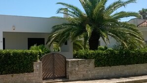 A modern building with a gated entrance, a palm tree, and a hedge.