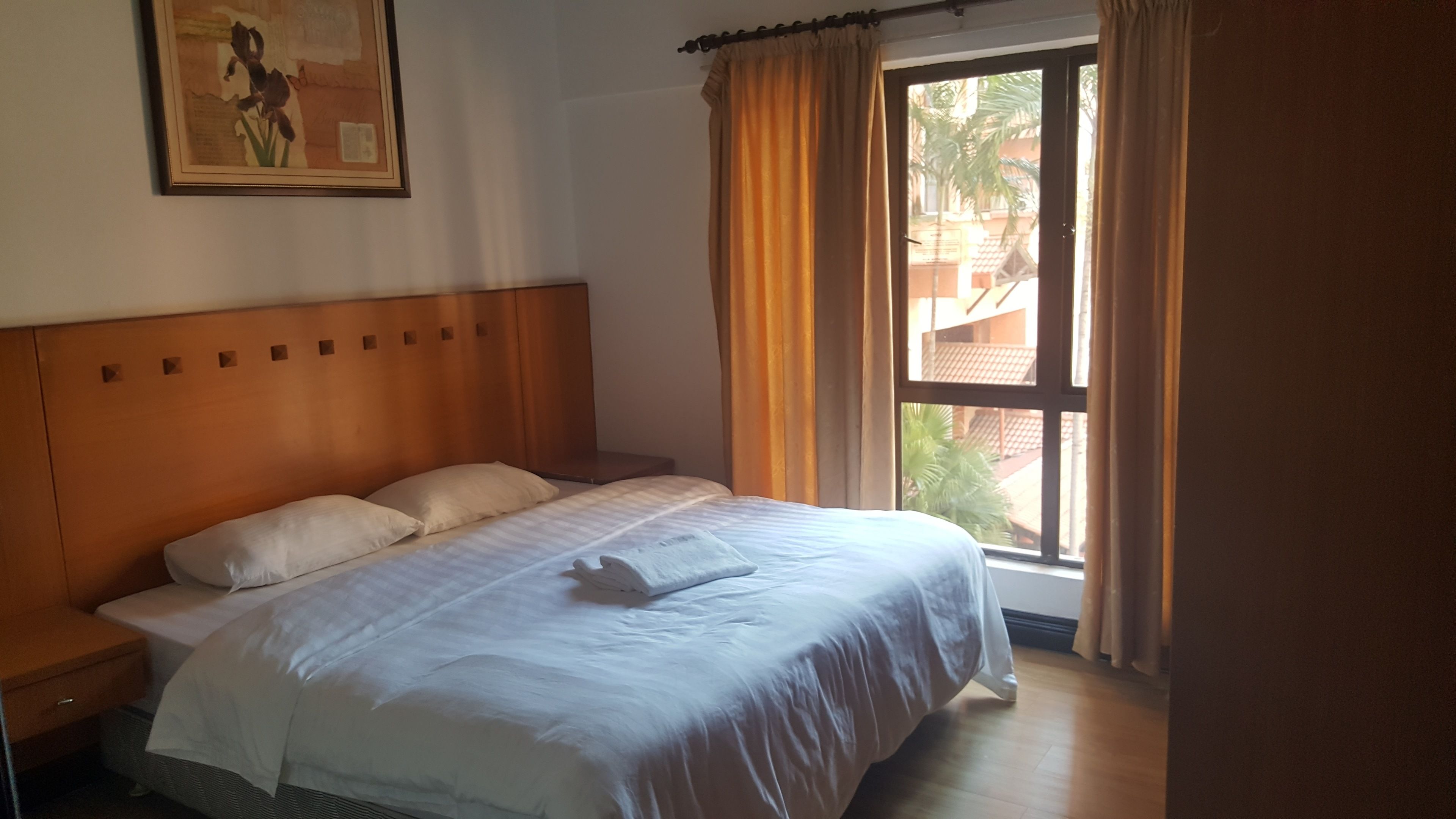 A hotel room with a bed, a nightstand, a window with curtains, and a framed picture on the wall.