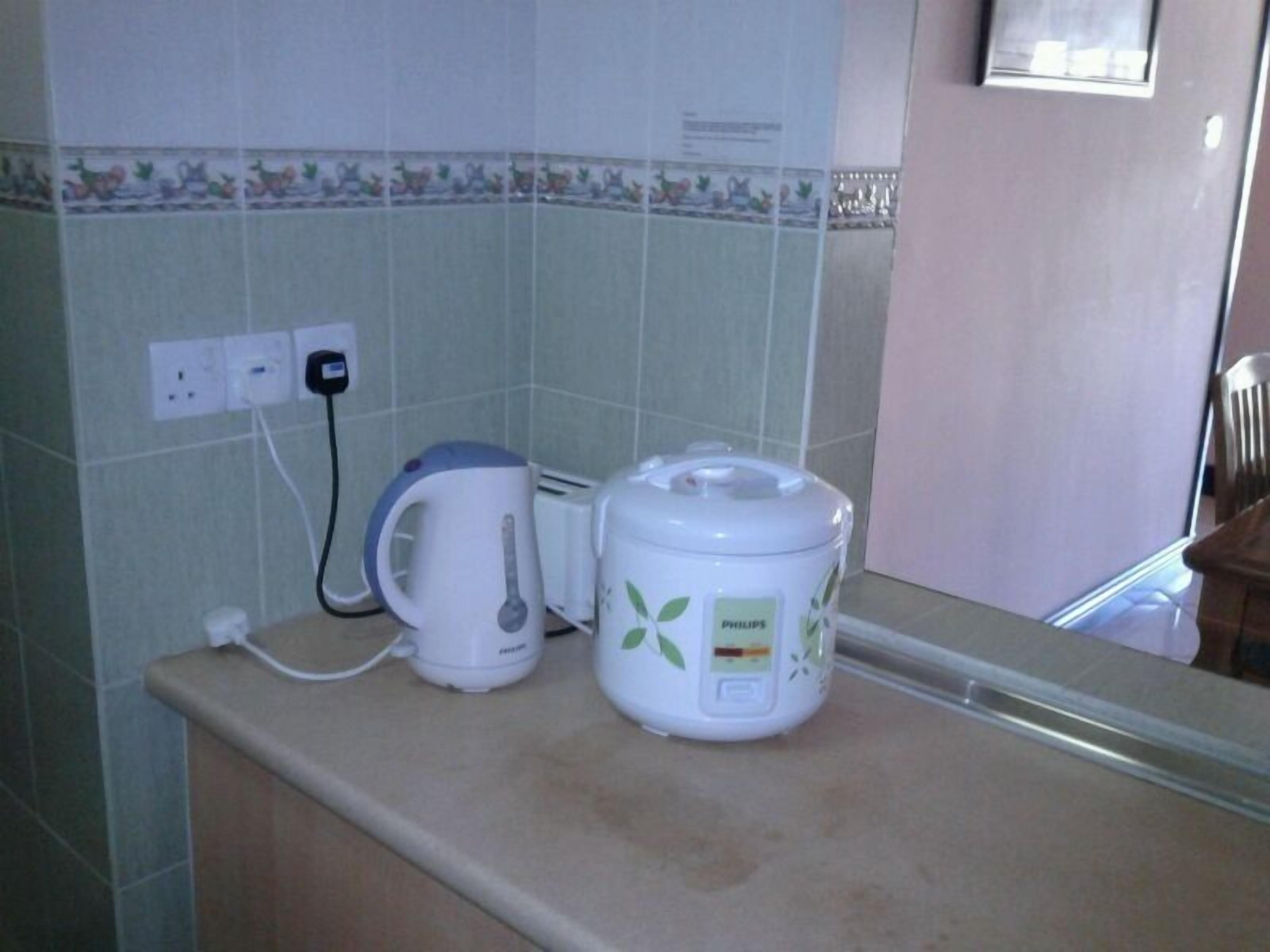Cozinha com cafeteira e chaleira na bancada, tomada e painel de azulejos.