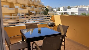 A balcony with a table, chairs, a grill, and a glass of drink.