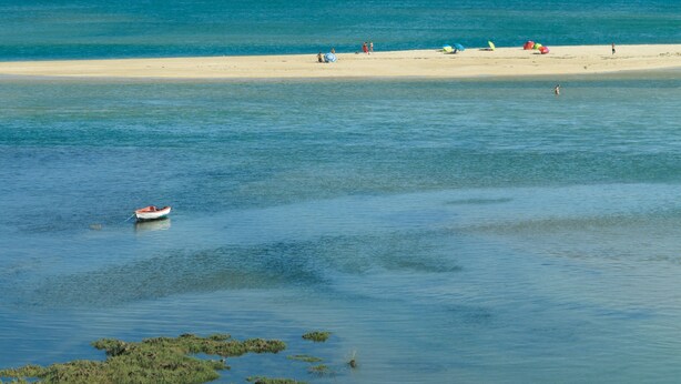 A beach with clear water, a boat, and people on the sand.