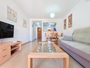 A living room with a flat-screen TV, wooden coffee table, sofa, and dining area with chairs.