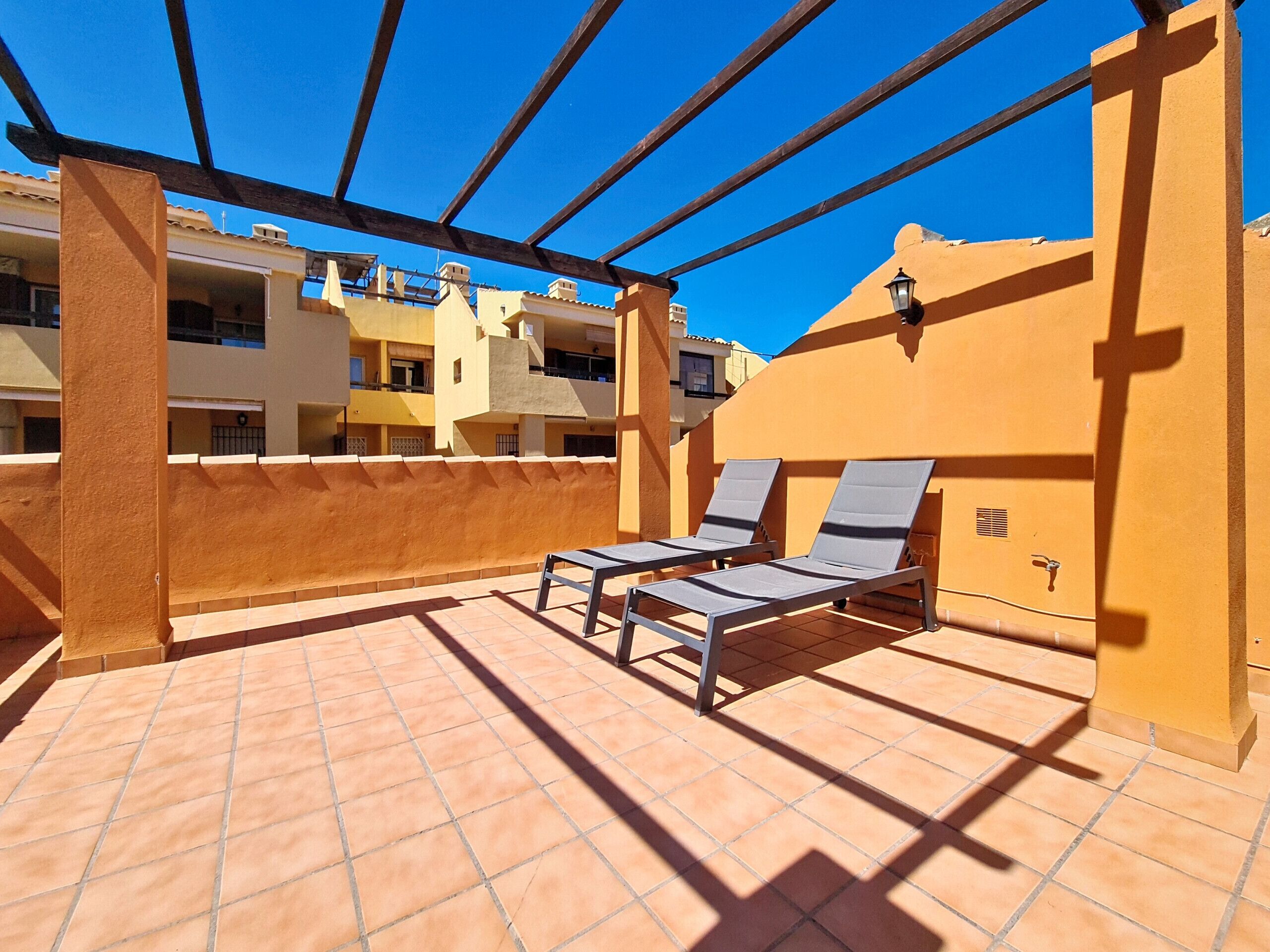 Eine Dachterrasse mit zwei Liegestühlen, einer Pergola und Blick auf umliegende Gebäude.