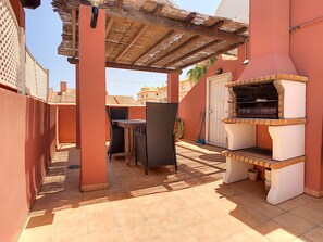 Une terrasse extérieure avec une table et des chaises, un barbecue et une pergola.