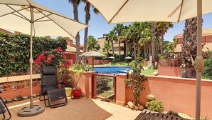 Un patio con mobiliario exterior, piscina y palmeras.