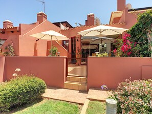 Une cour avec une porte, des plantes en pot et des parasols d’extérieur.
