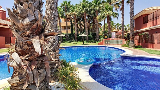 Una piscina rodeada de palmeras y un edificio con techo de tejas.