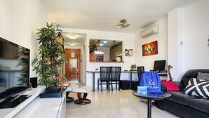 Una sala de estar moderna con una televisión de pantalla plana, un sofá, un comedor y una cocina al fondo.