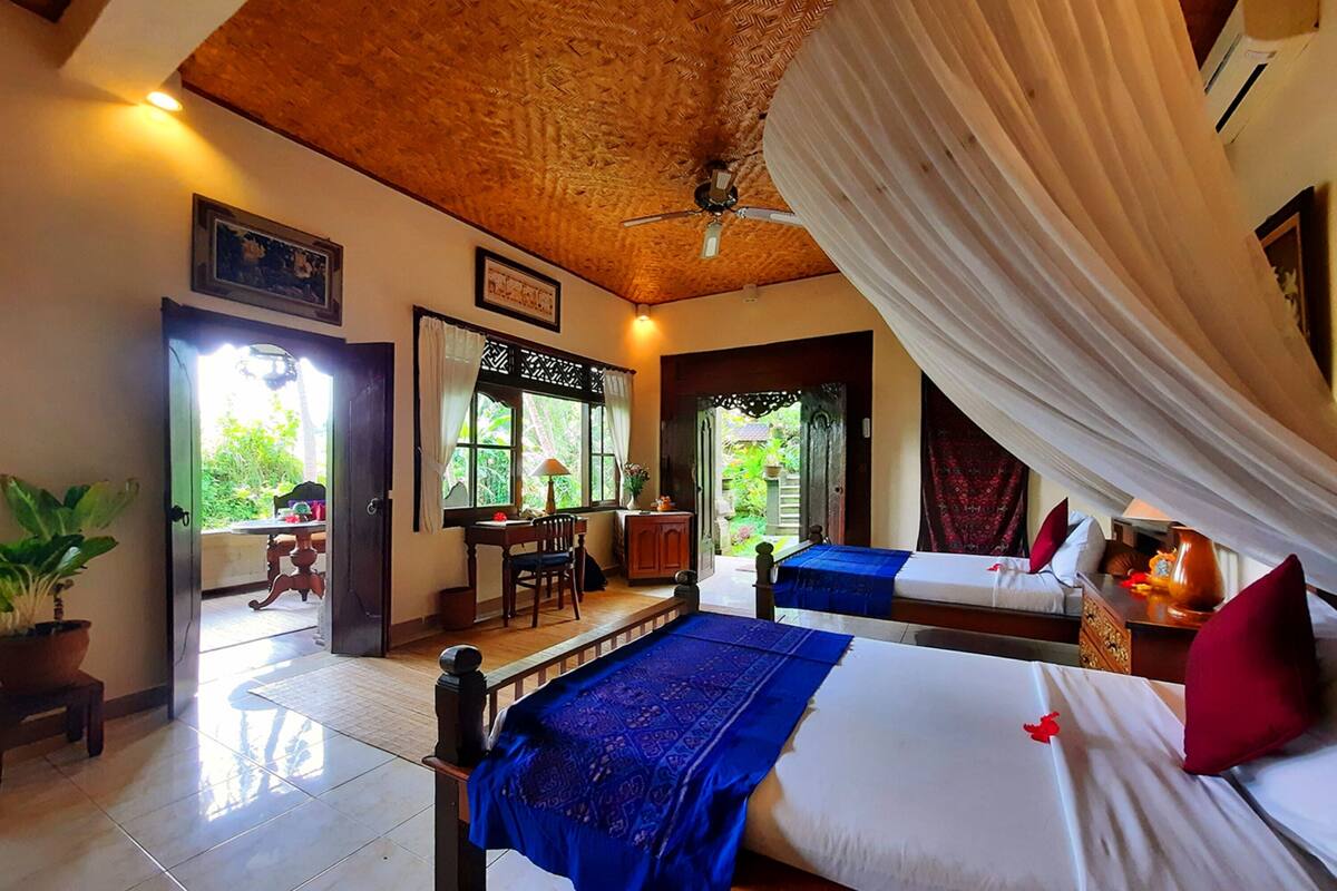 A room with two beds, a dining area, and a view of the garden.