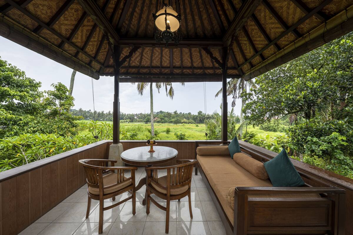A covered outdoor seating area with a table and chairs, overlooking a lush green landscape.