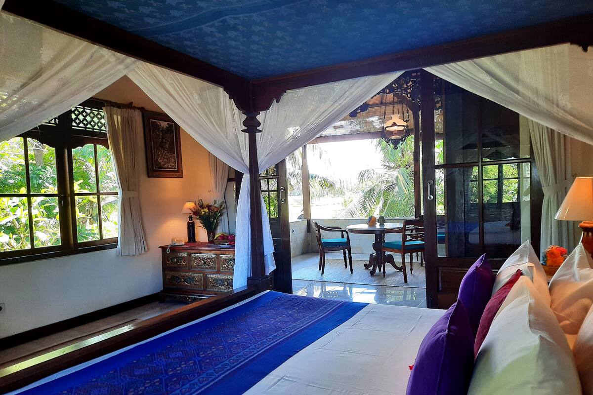 A room with a bed, a table, chairs, and a view of greenery outside.