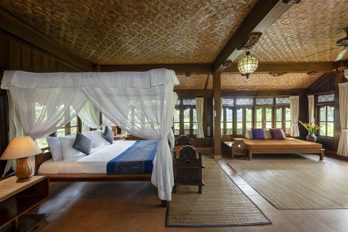 A room with a bed under a white canopy, a sofa with cushions, and a wooden table.