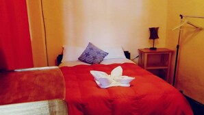 A hotel room with a bed, a nightstand, a lamp, and a red wall. - Little Home (Cusco)