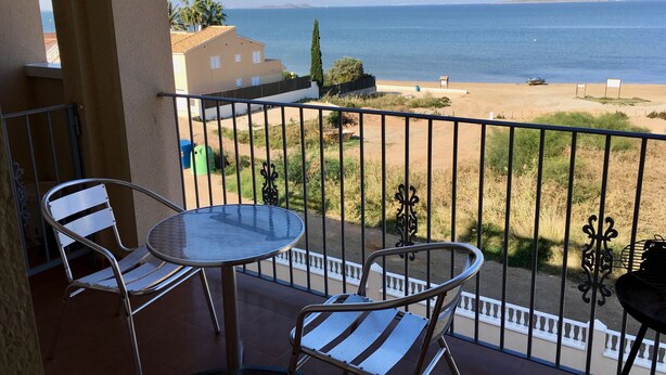 A balcony with two chairs and a table, overlooking a beach and the sea. - Front line sea view penthouse apartment, roof terrace, communal pool (Los Nietos)