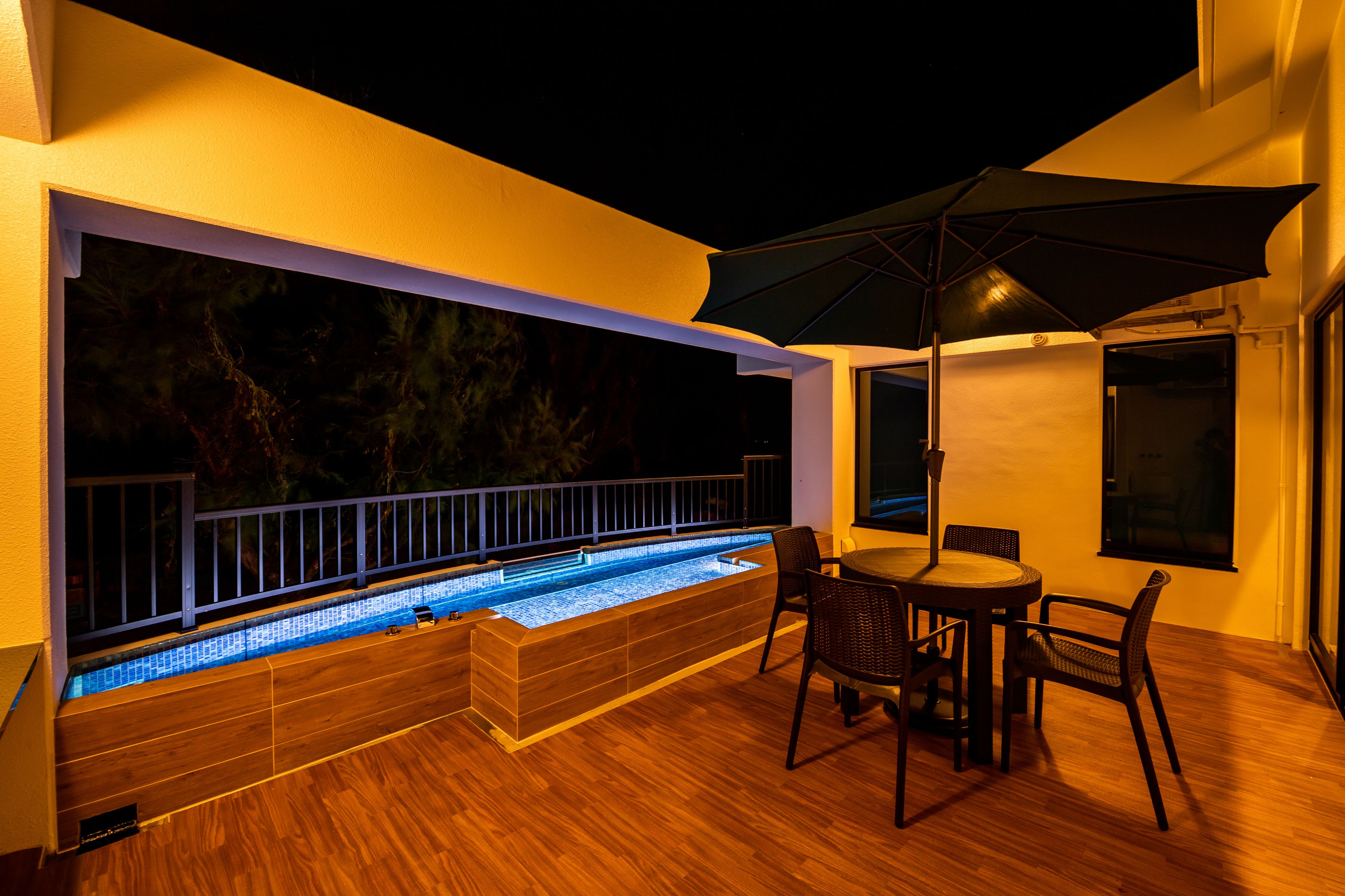 Une terrasse extérieure moderne dotée d’une piscine chauffée, d’une terrasse en bois et d’un coin repas avec des chaises et un parasol.