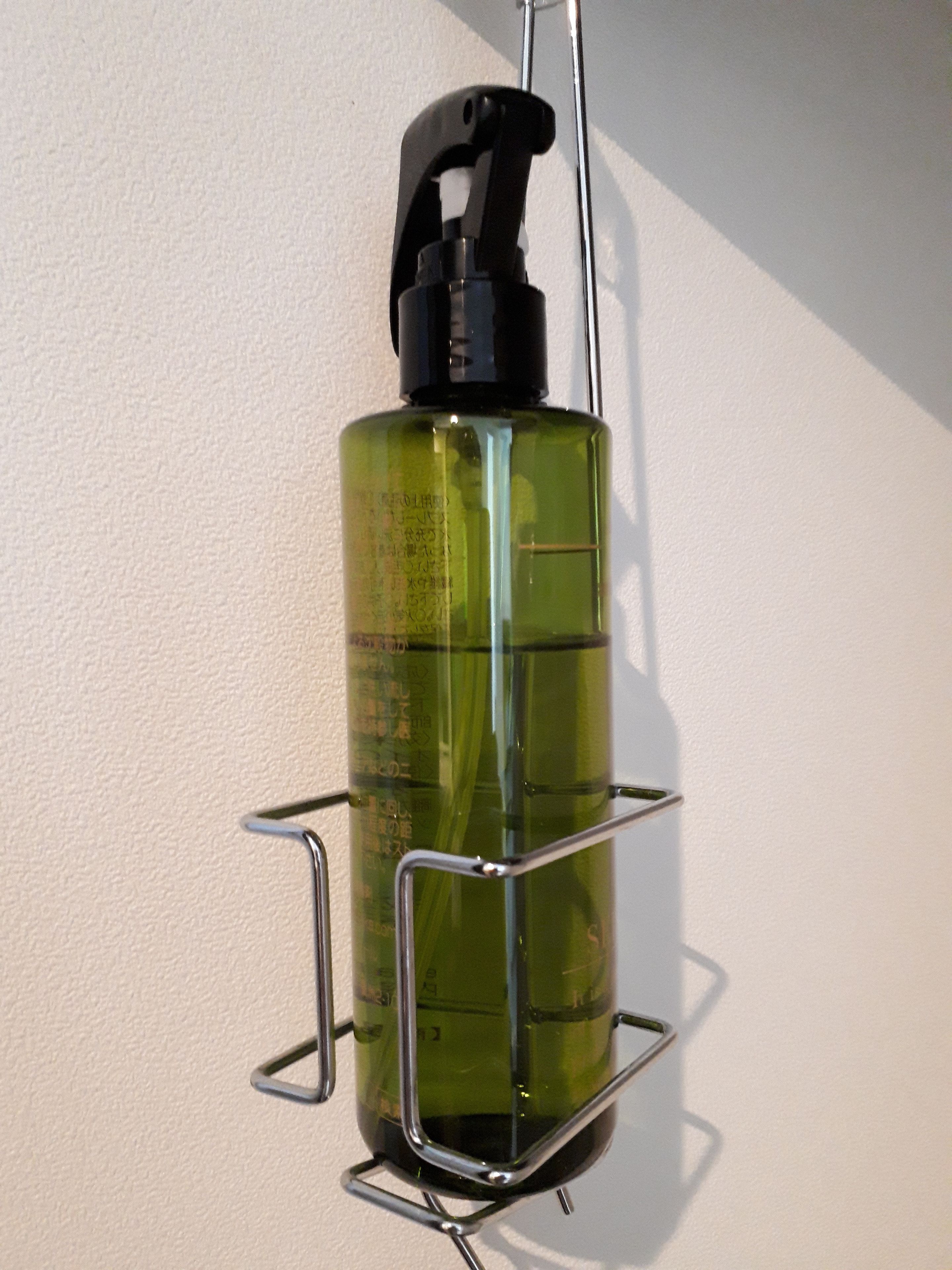 A green spray bottle mounted on a metal rack against a white wall.