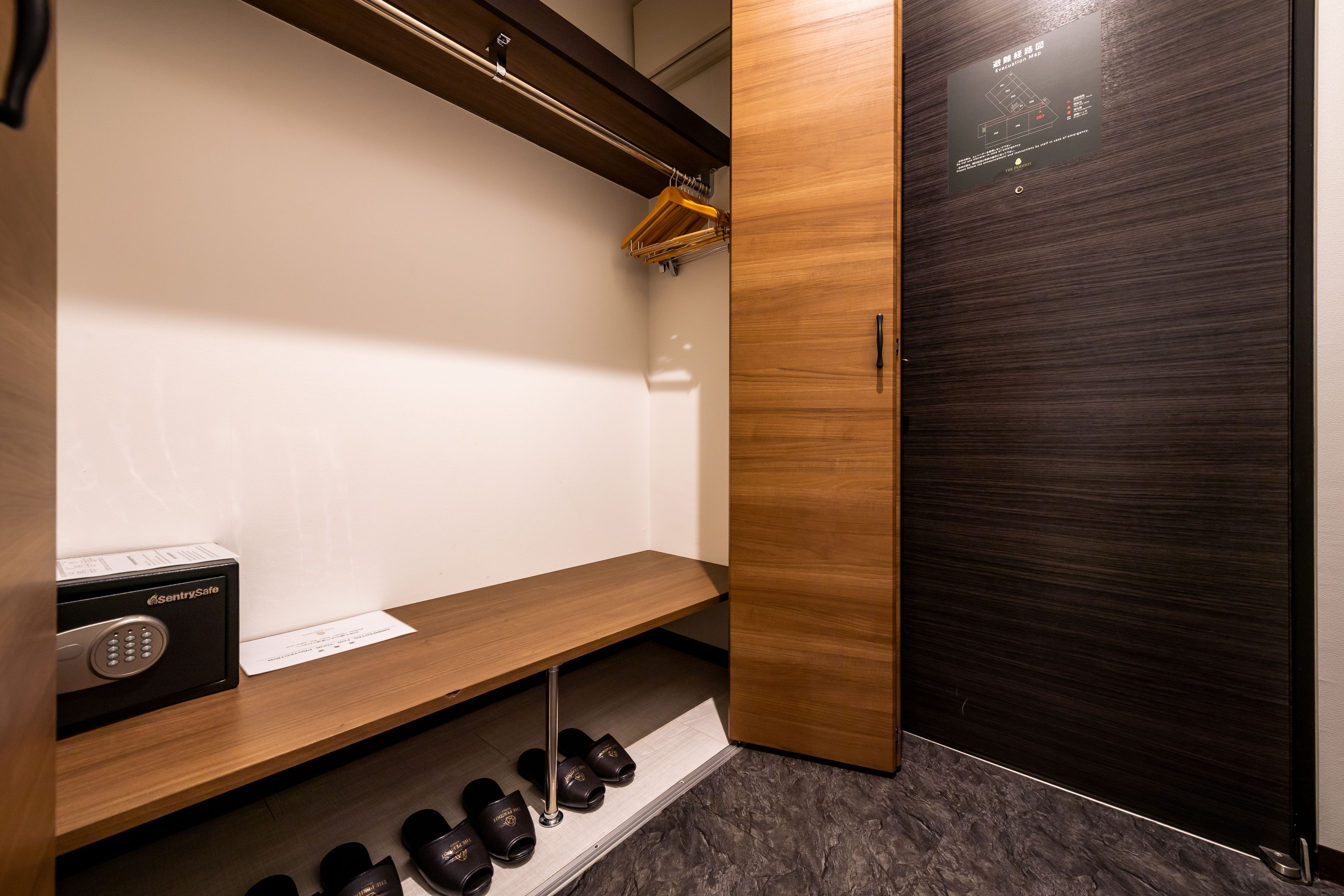 A modern closet with a wooden shelf, a shoe rack, and a black safe.