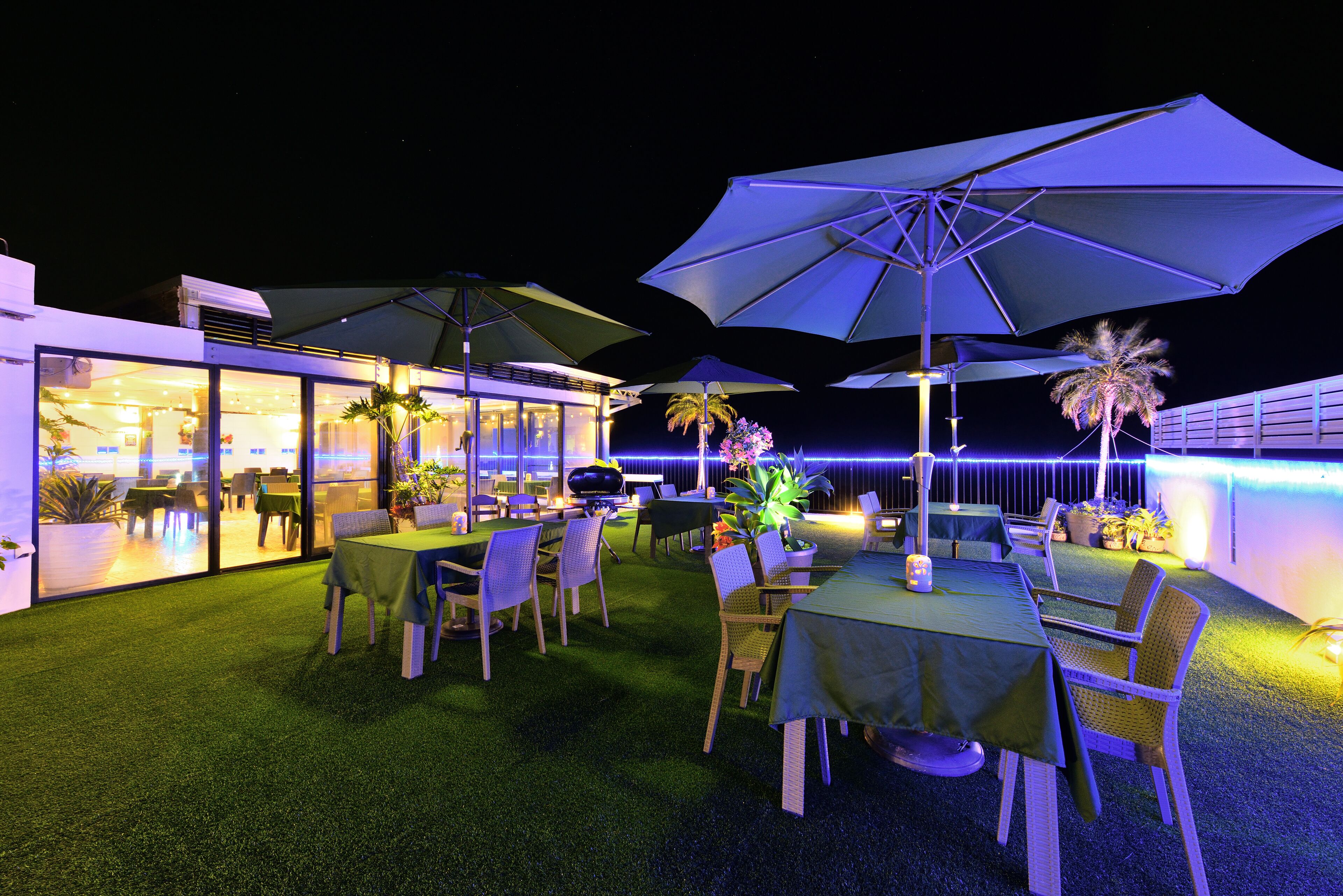 An outdoor dining area with tables and chairs, umbrellas, and a pool in the background.