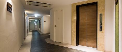 A hotel hallway with a marble floor, a wooden elevator, and a white door.