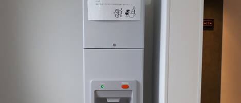 A white vending machine with a water dispenser, located in a hallway with a tiled floor.