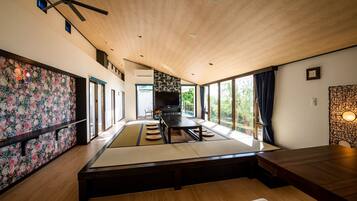 A modern interior with a wooden ceiling, tatami mats, a dining table, and a TV in the background.